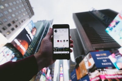 Hand holding a smartphone showing an Instagram profile against city buildings
